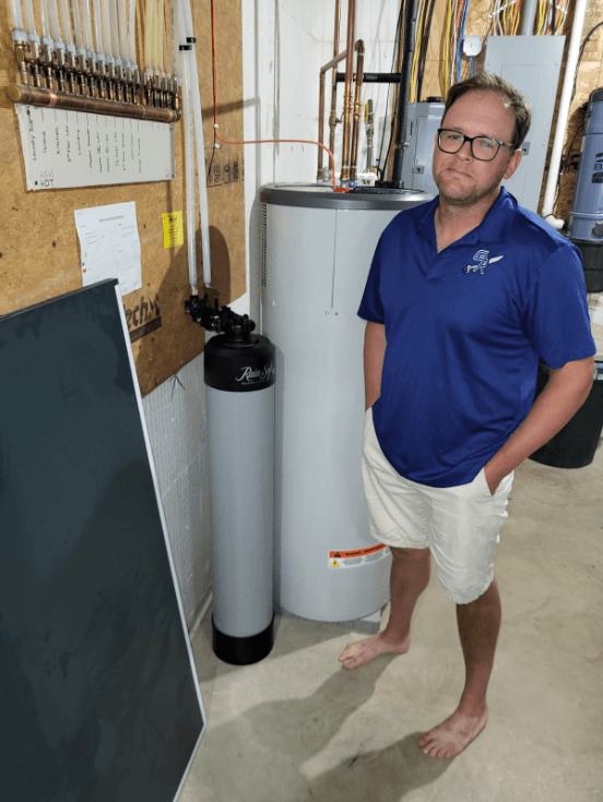 Adam standing next to water heater and filtration system in utility room