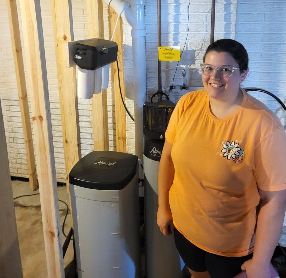 Person in yellow shirt standing next to water softening system equipment in basement installation area