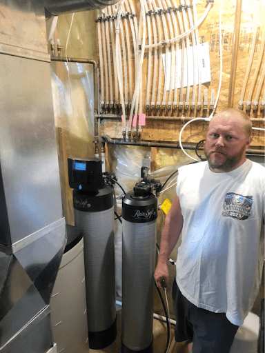 Man standing next to water filtration system equipment in workshop with tools hanging on wall behind him