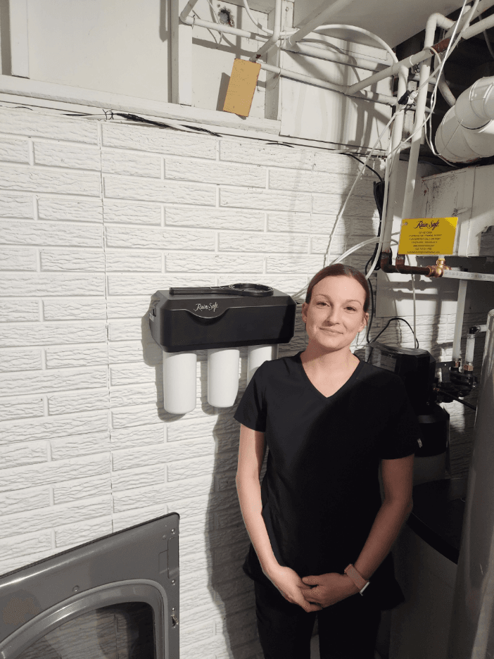 Woman standing in laundry room next to wall-mounted water filtration system and dryer