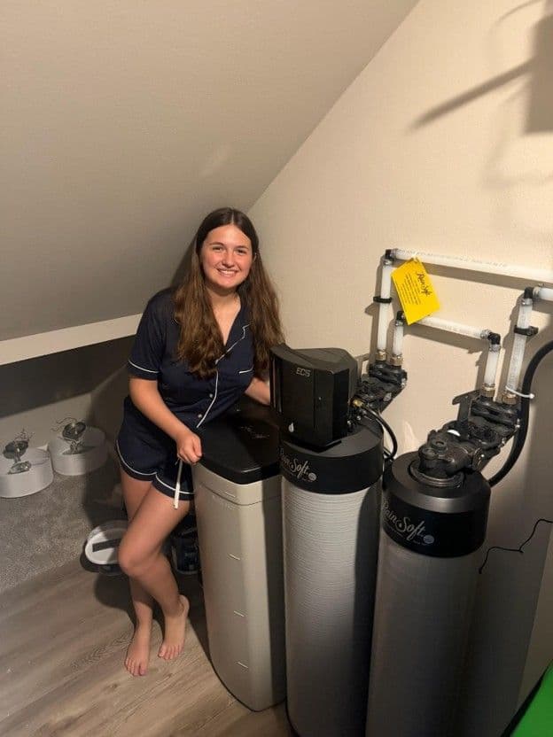 Woman smiling next to water filtration system tanks and 3D printer in utility room