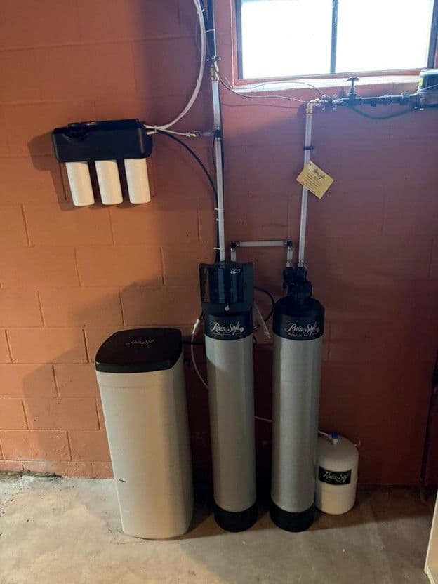 Water softening system with two cylindrical tanks, brine tank, and control valve mounted against brick wall in basement