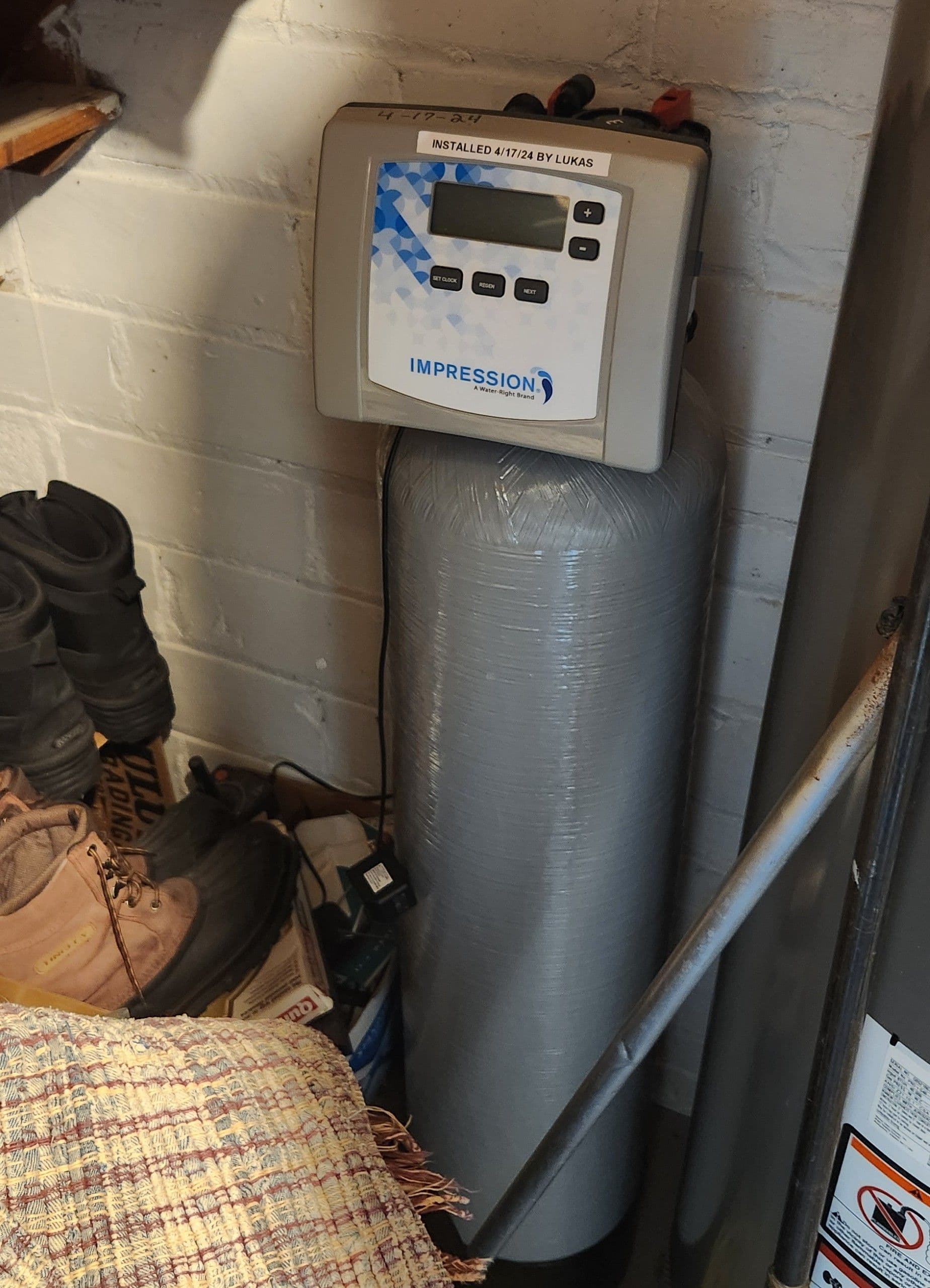 Impression water softener system installed on basement wall with digital control panel displaying time and settings, installed April 2024 by Lukas