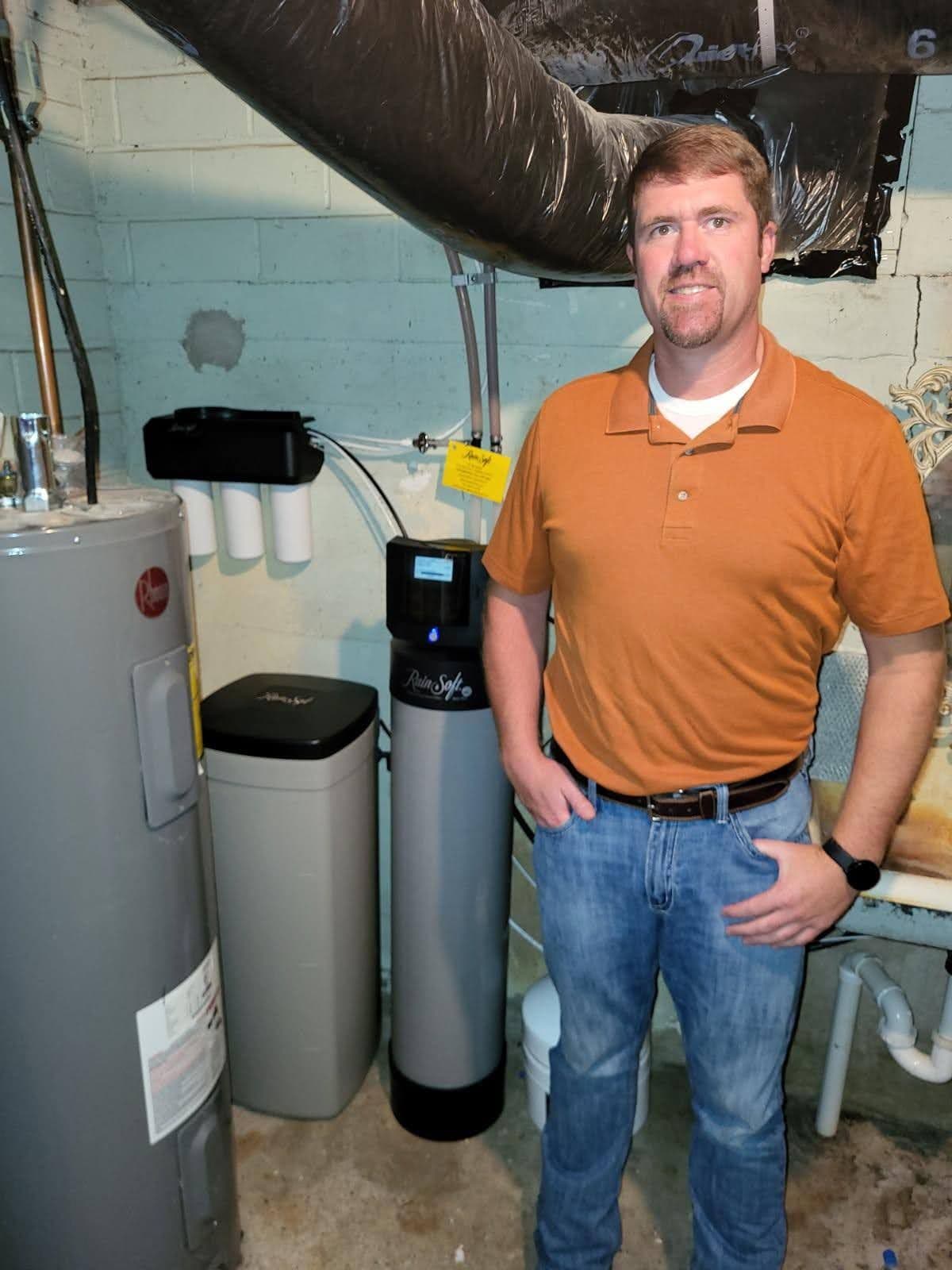 Tom standing next to water softener and filtration system equipment in basement mechanical room