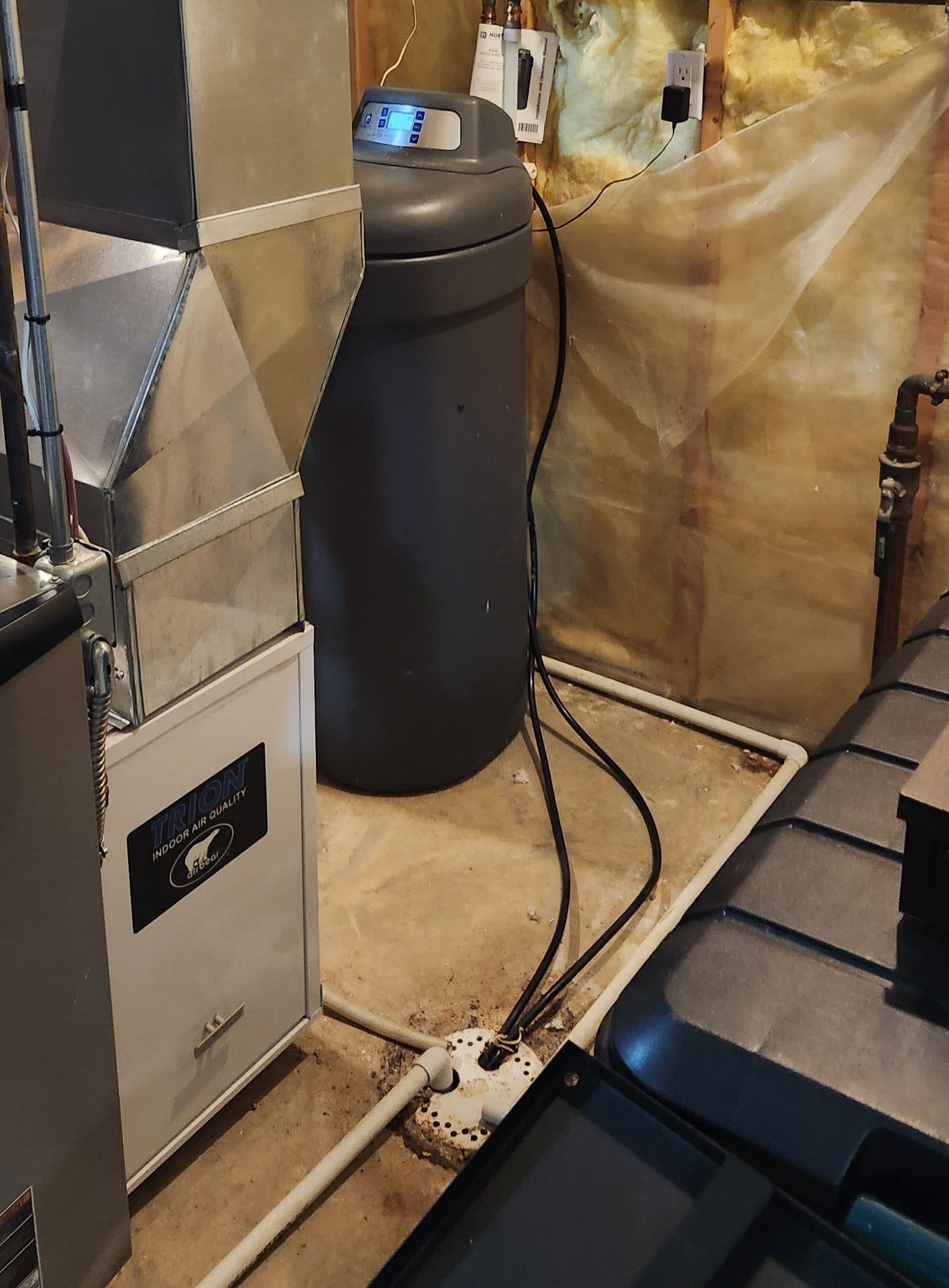 Water softener system with digital display connected to power outlet and plumbing in basement utility room